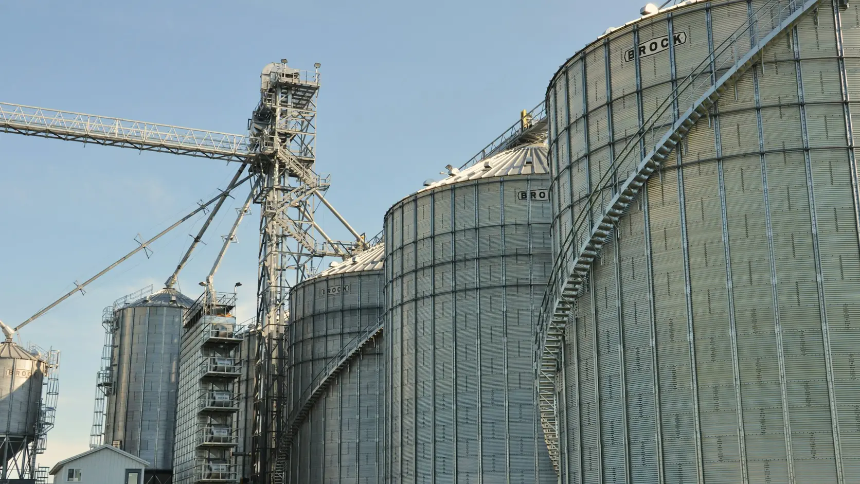 Planta de alimentos moderna con silos de acero y sistemas de transportadores bajo un cielo despejado.